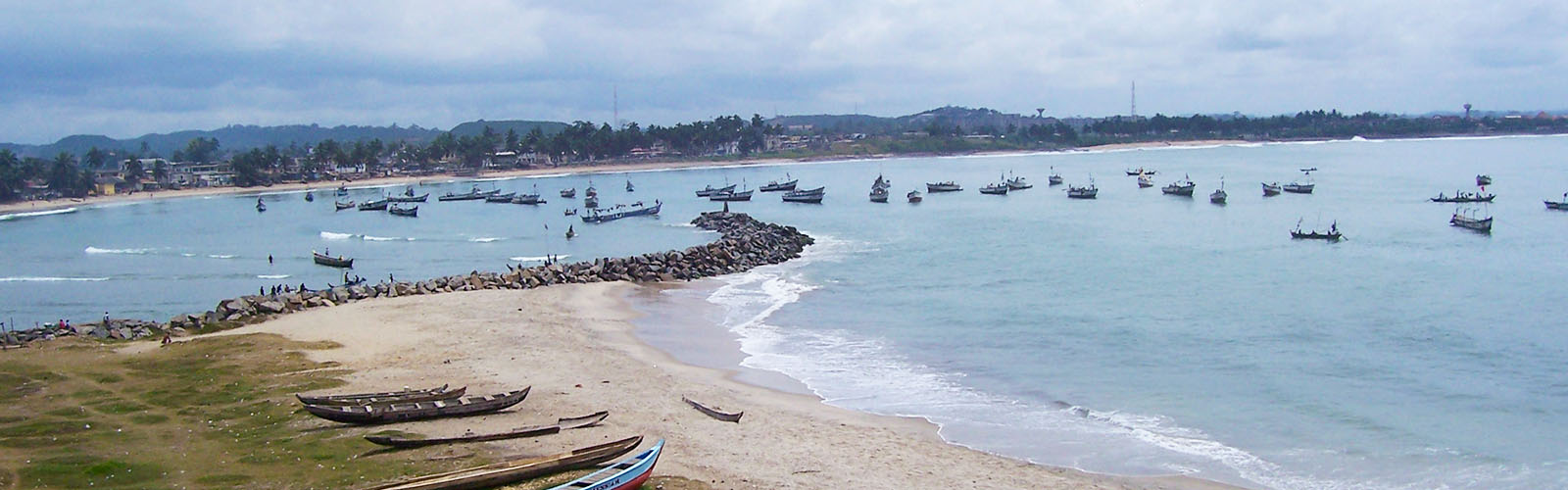 Coast of Legon with waves coming onto the sand and multiple boats in the background on the water.